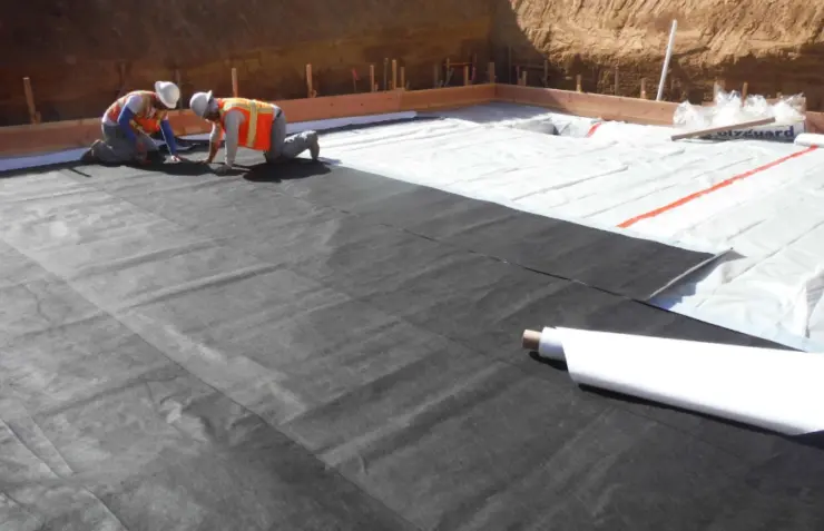 Workers installing below-grade sheet waterproofing membrane.