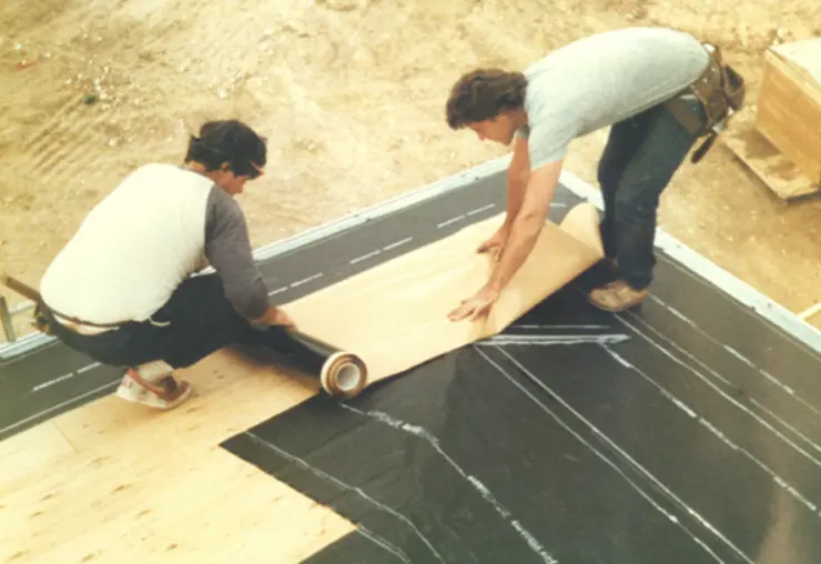 Workers install a peel and stick vapor barrier material.