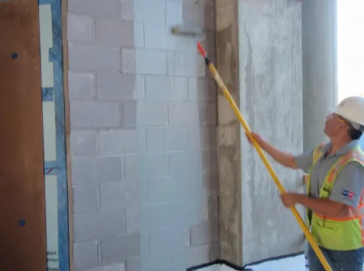Worker applying cementitious waterproofing coating to a concrete wall.