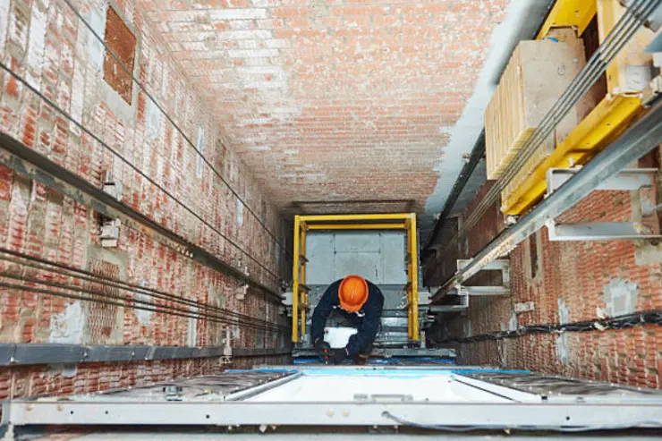Construction worker wearing an orange hard hat working inside a brick elevator shaft.